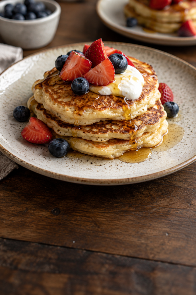 Pancakes topped with strawberries, blueberries, yogurt and maple syrup.